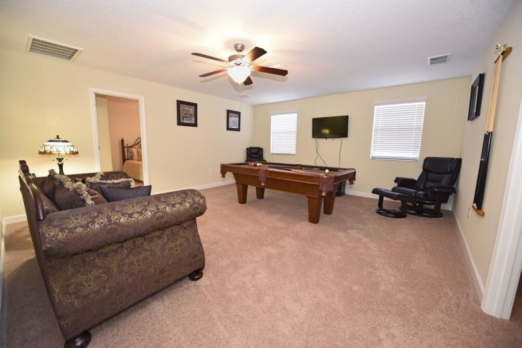 A living room with a pool table, a ceiling fan, a sofa, and a TV mounted on the wall.