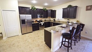 A modern kitchen with dark cabinets, stainless steel appliances, and a central island with bar stools. - 2341 Providence House 6 Bedroom by Florida Star (Davenport)