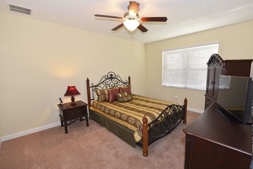 A bedroom with a bed, a nightstand, a lamp, a ceiling fan, a window with blinds, and a dresser.