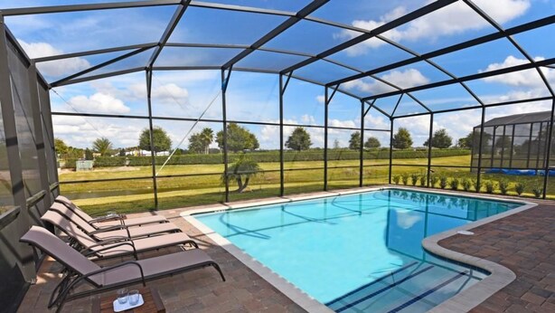 A covered swimming pool with lounge chairs and a table, surrounded by a metal fence and brick flooring. - 2383 Providence House 6 Bedroom by Florida Star (Davenport)
