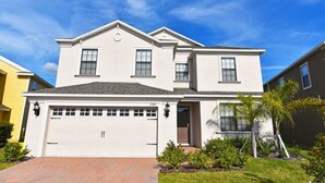 A two-story house with a white garage door, a front entrance, and a small garden with a palm tree. - 2383 Providence House 6 Bedroom by Florida Star (Davenport)