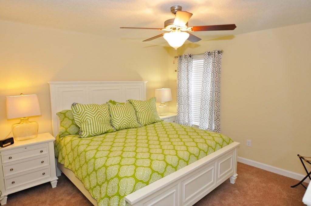 A bedroom with a bed, nightstands, a ceiling fan, and patterned curtains.