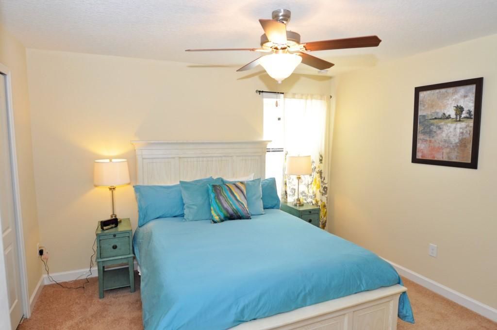 A bedroom with a bed, two bedside tables, a ceiling fan, and a window with curtains.