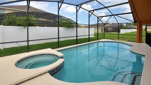 Ein Swimmingpool mit Whirlpool, umgeben von einer überdachten Fläche mit weißem Zaun und Häusern im Hintergrund.