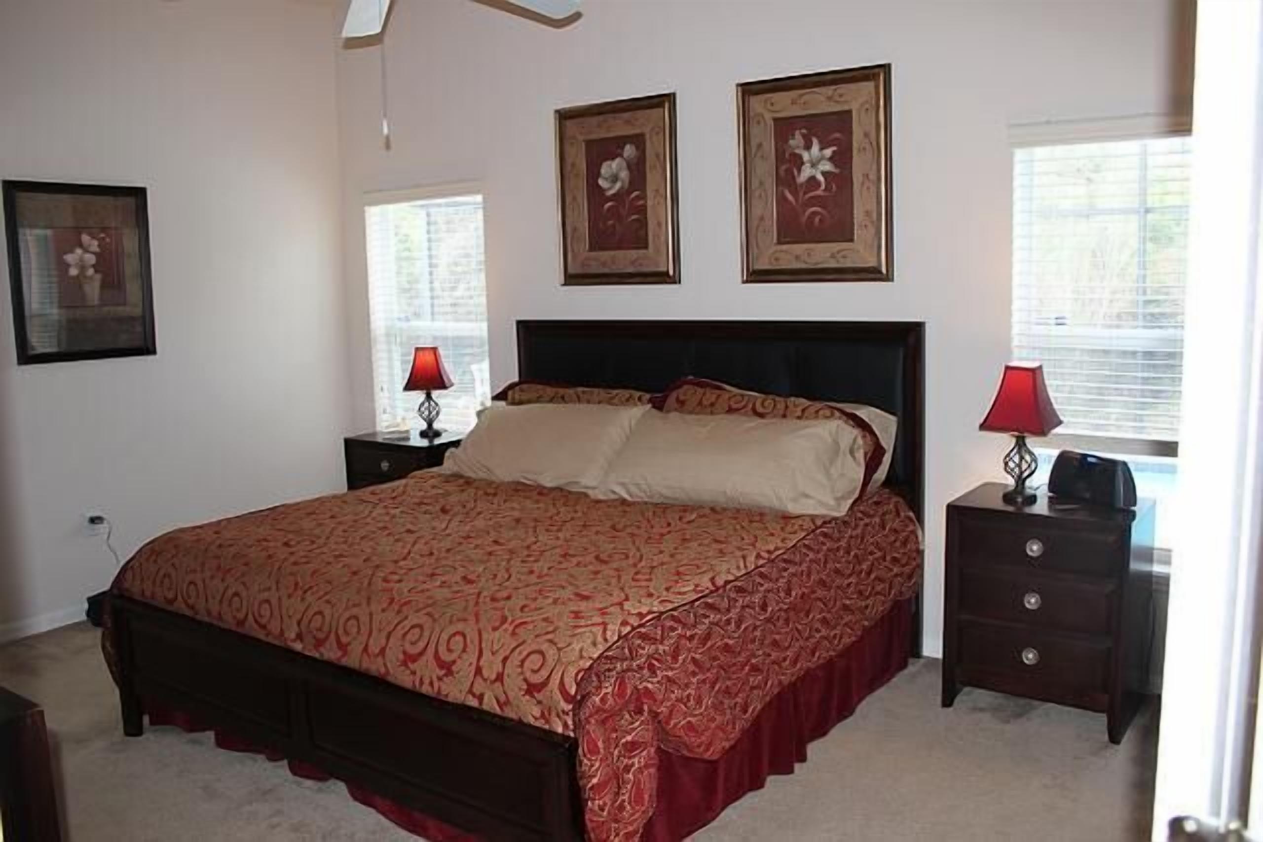 A bedroom with a large bed, two nightstands, and framed pictures on the wall.