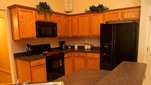 A compact kitchen with wooden cabinets, a black microwave, a black refrigerator, and a granite countertop. - 251 Sandy Ridge House 4 Bedroom by Florida Star (Davenport)