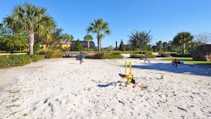 Hiekkainen ranta-alue, jossa on leikkivälineitä ja palmuja.
