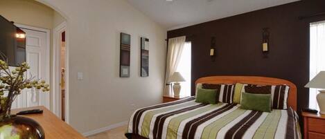 A bedroom with a bed, a nightstand, a desk, and a ceiling fan.