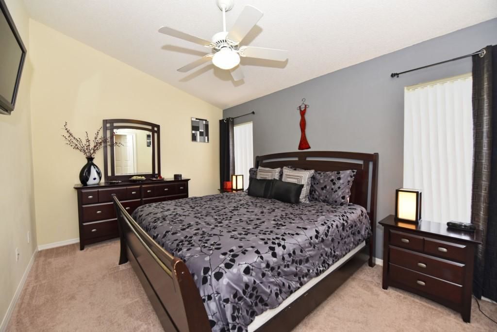 A bedroom with a bed, a nightstand, a dresser, a mirror, a ceiling fan, and a window with curtains.