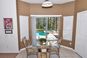 A dining area with a glass table and chairs, a view of a swimming pool, and a door to the right.