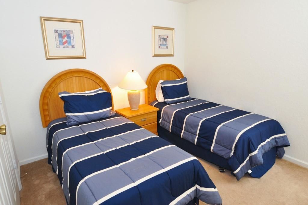 A bedroom with two single beds, each with a wooden headboard, a bedside table with a lamp, and framed pictures on the wall.