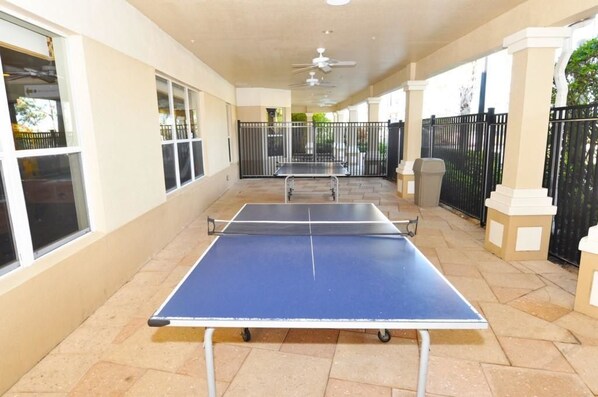 An outdoor area with two ping pong tables, a covered walkway, and a view of the surrounding area.