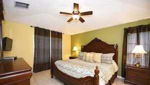 Un dormitorio con una cama de madera, dos mesitas de noche con lámparas, un ventilador de techo y un televisor sobre un mueble.