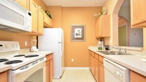 A compact kitchen with white appliances, wooden cabinets, and a tiled floor. - 2809 Windsor Hills Condo 3 Bedroom by Florida Star (Kissimmee)