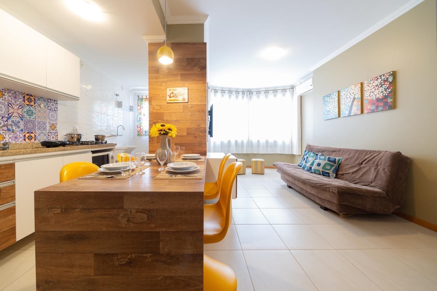 Una cucina moderna con isola in legno, zona pranzo con sedie gialle e un soggiorno con divano marrone.