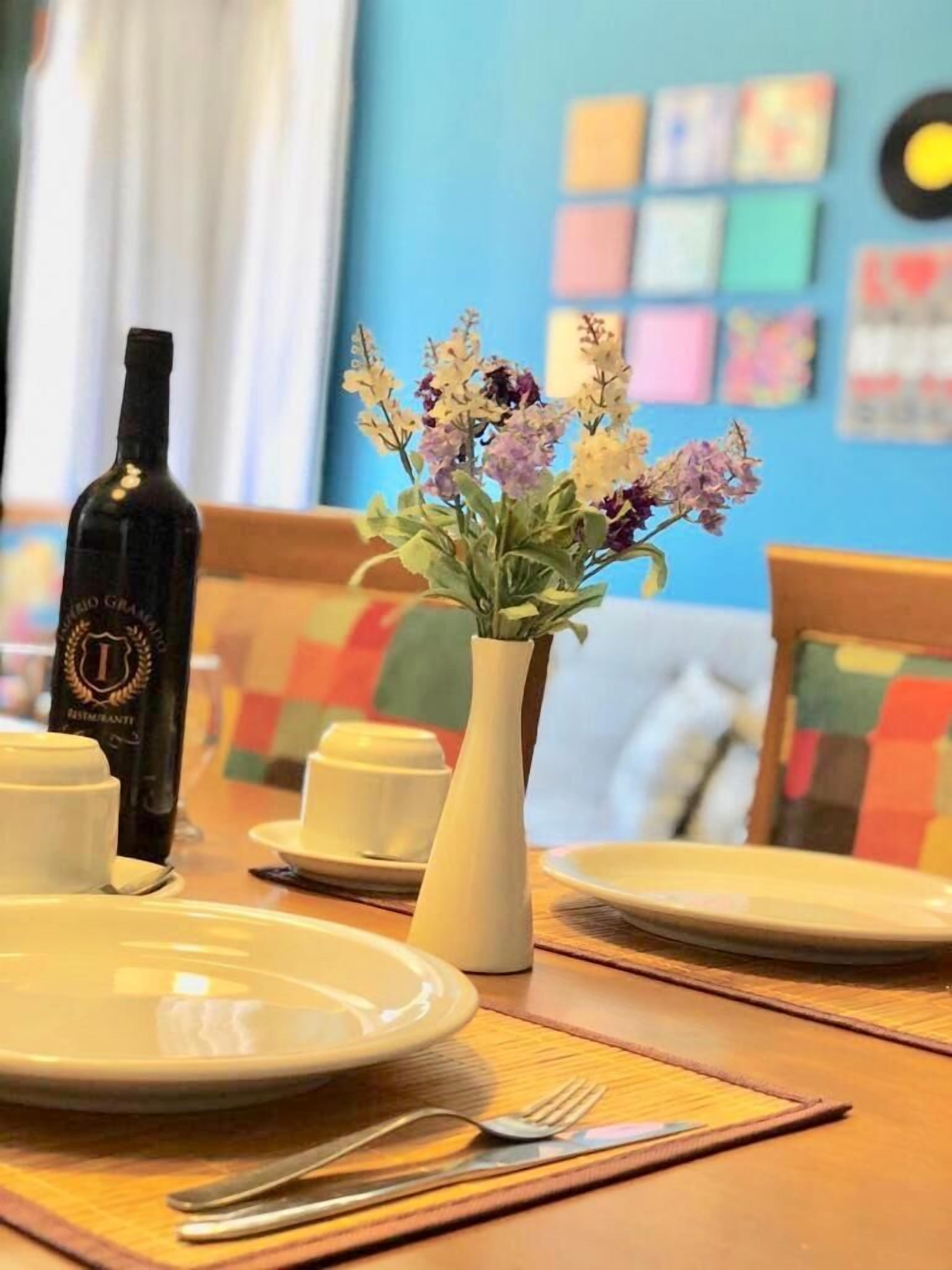 A dining table with plates, cutlery, a bottle, and a vase with flowers.