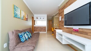Uma sala de estar com sofá, televisão de tela plana e área de jantar com cadeiras e mesa.