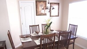 Comedor con una mesa de madera y seis sillas. Se ve una puerta y dos cuadros en la pared.