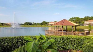 A gazebo by a lake with a fountain, surrounded by greenery and houses in the background. - 3010 Encantada House 4 Bedroom by Florida Star (Kissimmee)