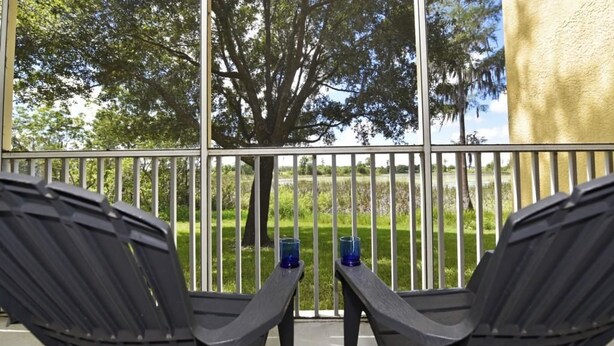 A balcony with two chairs and two blue glasses on a table, overlooking a grassy area with trees. - 3117 Sun Lake Condo 3 Bedroom by Florida Star (Kissimmee)