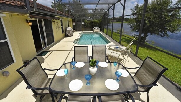 An outdoor pool area with a covered patio, a table set for dining, and a view of a lake. - 3125 VillaSol Townhome 4 Bedroom by Florida Star (Kissimmee)