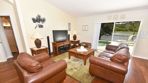 A living room with leather sofas, a coffee table, a TV, and a view of a pool through a sliding glass door. - 3125 VillaSol Townhome 4 Bedroom by Florida Star (Kissimmee)