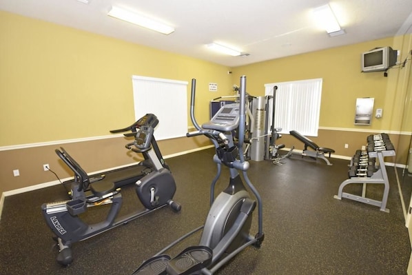 Un gimnasio con máquinas de cardio, bancos de pesas y mancuernas.