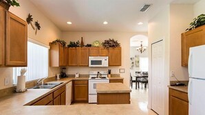 A modern kitchen with wooden cabinets, a white stove, a microwave, and a dining area with a chandelier. - 320 High Grove House 5 Bedroom by Florida Star (Clermont)