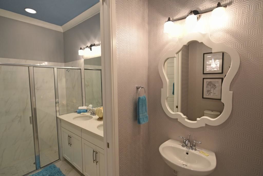 Un baño con cabina de ducha de vidrio, tocador con lavabo y un espejo grande con marco original.