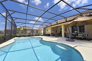 Una piscina interior con cerramiento de vidrio, sillas de descanso y un patio con mobiliario exterior.