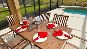 A dining table set for four with red napkins, white plates, and a vase of flowers. - 4183 Solterra House 6 Bedroom by Florida Star (Davenport)