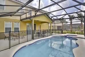 A swimming pool with a glass enclosure, surrounded by lounge chairs and a covered patio area.