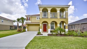 A two-story residential building with a red door, a balcony on the second floor, and a well-maintained lawn. - 4184 Solterra House 6 Bedroom by Florida Star (Davenport)