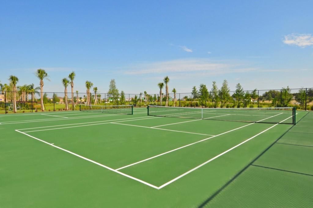 Una cancha de tenis con red, rodeada de palmeras y cielo despejado.