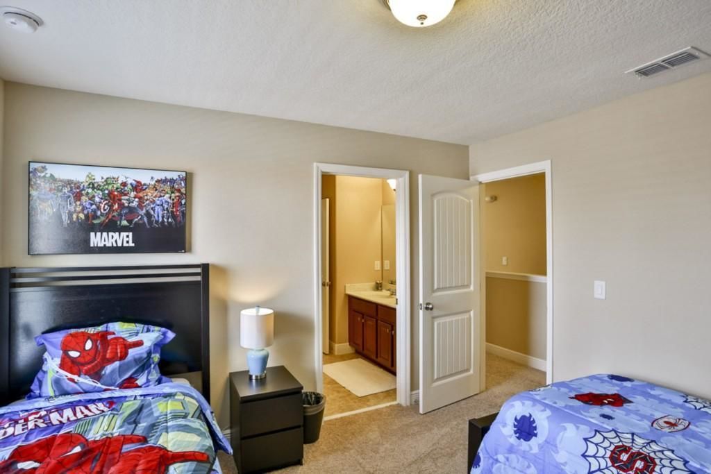 A bedroom with a bed featuring a Spider-Man themed bedspread, a wall-mounted Spider-Man poster, and a nightstand with a lamp.