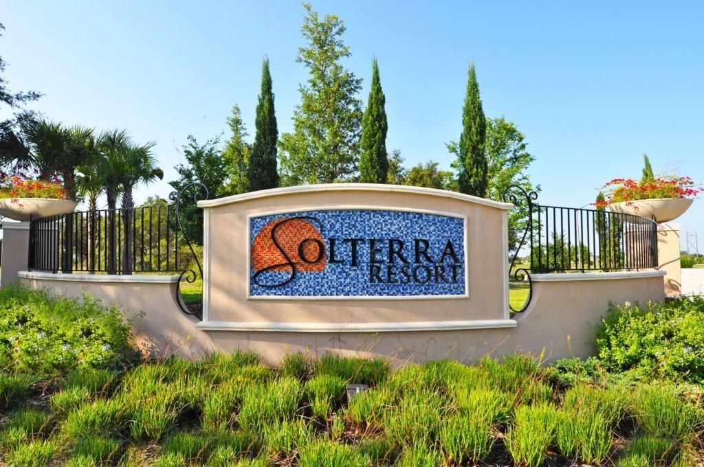 A sign for Solterra Resort with a mosaic design, surrounded by greenery and a fence.