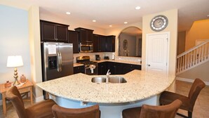 A kitchen with dark cabinets, stainless steel appliances, a granite countertop, and a sink. - 4425 Solterra House 5 Bedroom by Florida Star (Davenport)