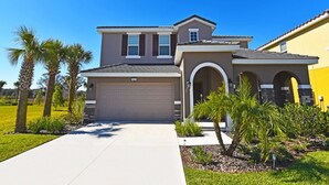 A two-story house with a garage, a covered porch, and a landscaped front yard with palm trees. - 4425 Solterra House 5 Bedroom by Florida Star (Davenport)