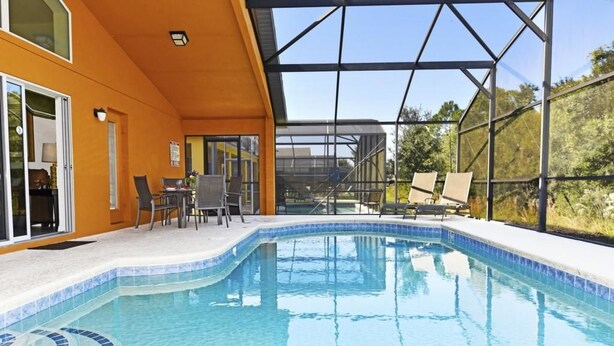 A swimming pool with a glass enclosure, a patio area with chairs, and a view of the surrounding landscape. - 4452 Veranda Palms House 4 Bedroom by Florida Star (Kissimmee)