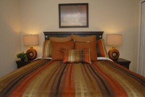 A bed with a striped bedspread, two bedside lamps, and a framed picture above the bed. - 4464 Veranda Palms House 6 Bedroom by Florida Star (Kissimmee)