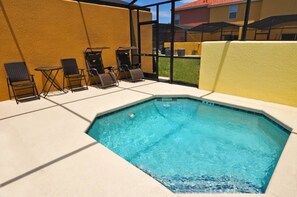 A swimming pool with lounge chairs and tables, surrounded by a yellow wall and a glass enclosure.