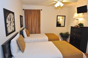 A hotel room with two beds, a ceiling fan, a TV, a dresser, and a mirror.