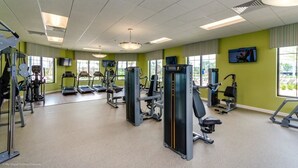 Une salle de sport équipée de divers appareils d’exercice, dotée de grandes fenêtres et d’un téléviseur fixé au mur.