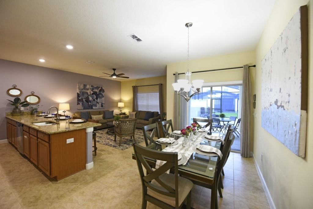 A spacious living area with a dining table, kitchen island, and a large window with curtains.