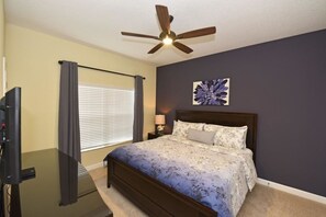 A bedroom with a bed, a ceiling fan, a TV, and a window with curtains.