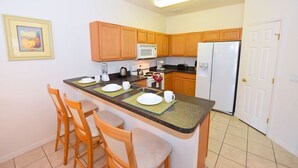 Una cocina compacta con armarios de madera, un microondas, un refrigerador y un pequeño comedor con sillas y una mesa.
