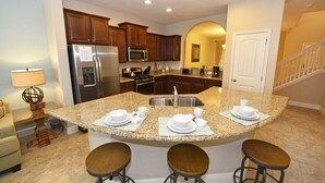 A kitchen with granite countertops, stainless steel appliances, and a central island with stools. - 5336 Solterra House 5 Bedroom by Florida Star (Davenport)