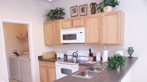 A compact kitchen with wooden cabinets, a microwave, a stove, and a sink. - 541 Sandy Ridge House 4 Bedroom by Florida Star (Davenport)