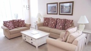 A living room with two beige sofas, a white coffee table, and a small side table with a lamp. There are two framed pictures on the wall. - 541 Sandy Ridge House 4 Bedroom by Florida Star (Davenport)