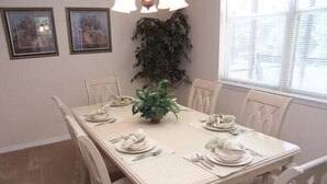 A dining table set for six with white chairs, a potted plant, and framed pictures on the wall. - 541 Sandy Ridge House 4 Bedroom by Florida Star (Davenport)